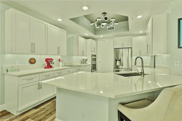 kitchen featuring sink, stainless steel appliances, a raised ceiling, light hardwood / wood-style flooring, and white cabinets