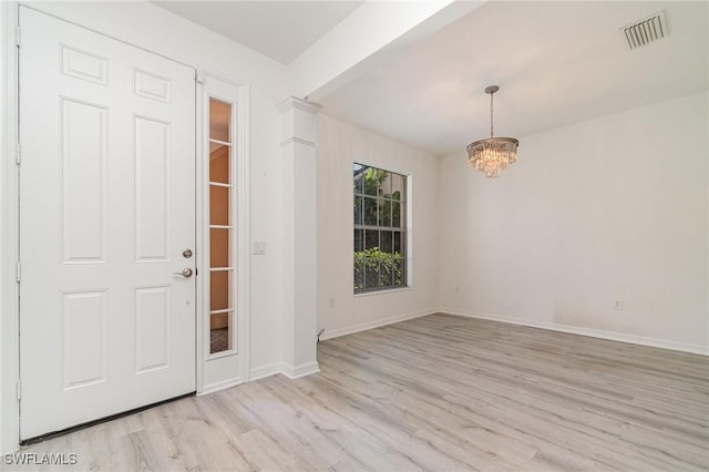 entryway with ornate columns, an inviting chandelier, and light wood-type flooring