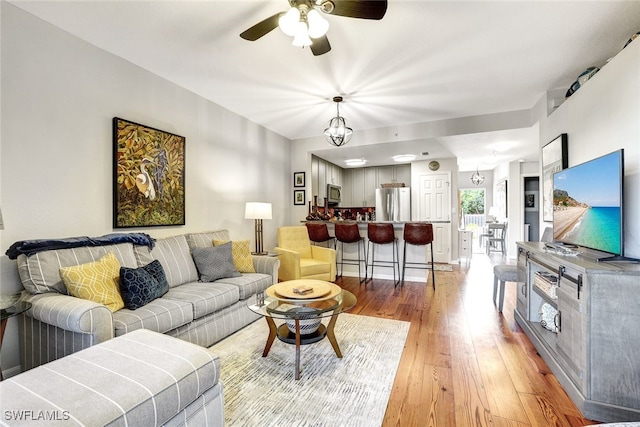 living area with light wood-type flooring and ceiling fan with notable chandelier