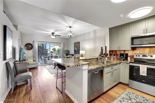 kitchen featuring stone countertops, open floor plan, a peninsula, stainless steel appliances, and a sink