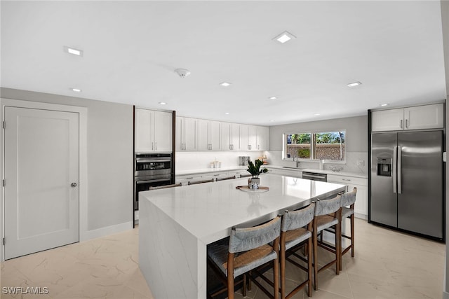 kitchen featuring a kitchen bar, a kitchen island, light stone counters, white cabinetry, and stainless steel appliances