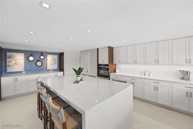 kitchen with a kitchen bar, white cabinets, decorative backsplash, a kitchen island, and light stone counters