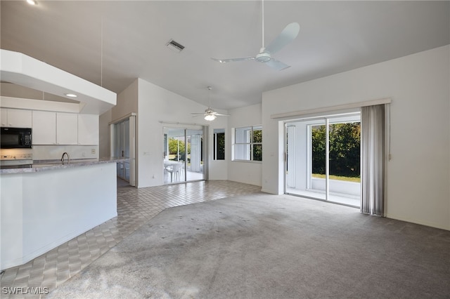 unfurnished living room featuring ceiling fan, plenty of natural light, light carpet, and vaulted ceiling