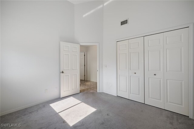 unfurnished bedroom with light carpet, a towering ceiling, and a closet