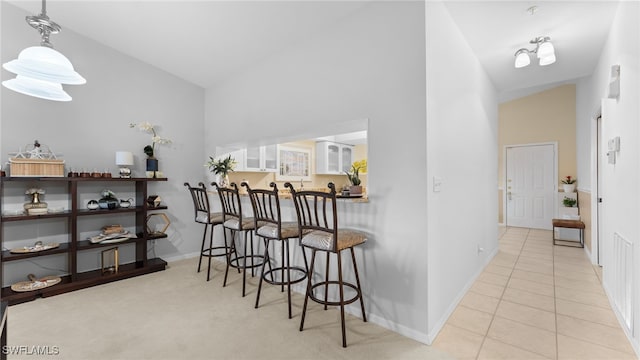 interior space with a kitchen breakfast bar, light tile patterned flooring, pendant lighting, and high vaulted ceiling