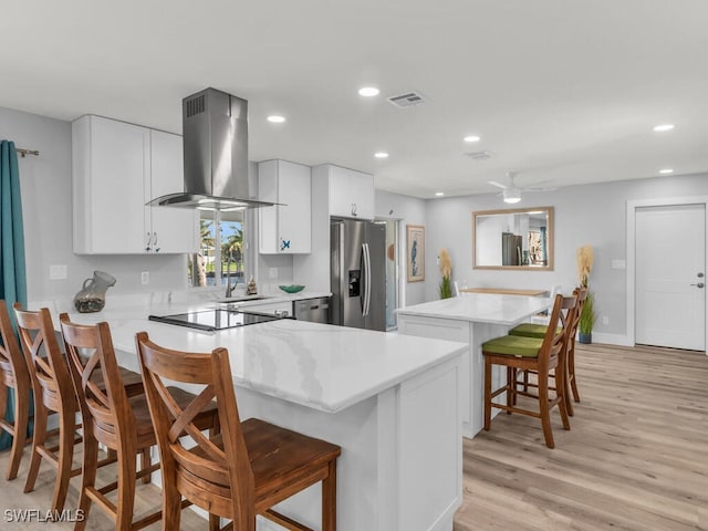 kitchen featuring white cabinets, a kitchen breakfast bar, wall chimney exhaust hood, light wood-type flooring, and stainless steel appliances