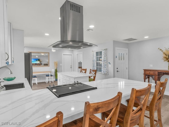 kitchen with island exhaust hood, white cabinets, light hardwood / wood-style flooring, and sink