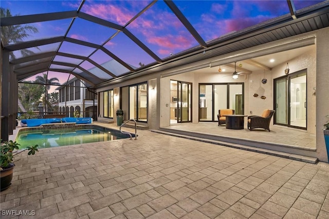 pool at dusk with glass enclosure, ceiling fan, a patio, and an outdoor hangout area