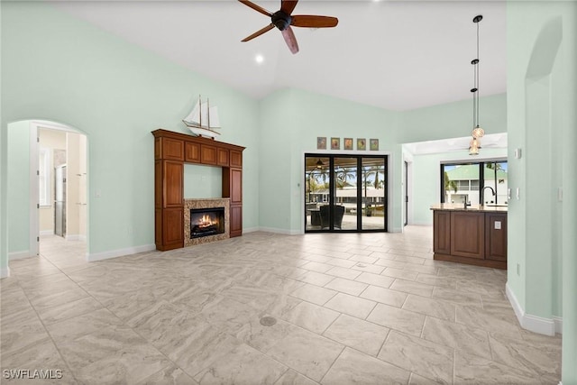 unfurnished living room with ceiling fan, sink, a fireplace, and a high ceiling