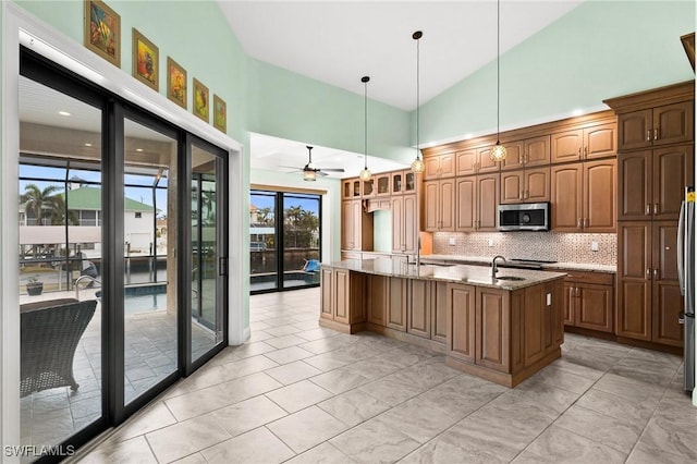 2405 Cherimoya Ln, Saint James City, FL 33956 - kitchen with stainless steel microwave, a center island with sink, light stone countertops, backsplash, and a ceiling fan