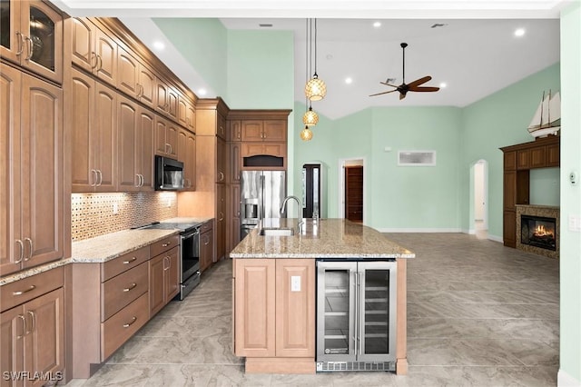 kitchen with wine cooler, an island with sink, appliances with stainless steel finishes, tasteful backsplash, and light stone counters