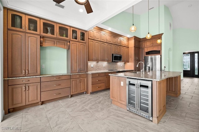 kitchen featuring appliances with stainless steel finishes, light stone counters, wine cooler, hanging light fixtures, and an island with sink