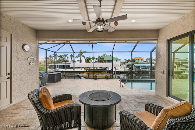 view of patio with ceiling fan, glass enclosure, and an outdoor living space with a fire pit