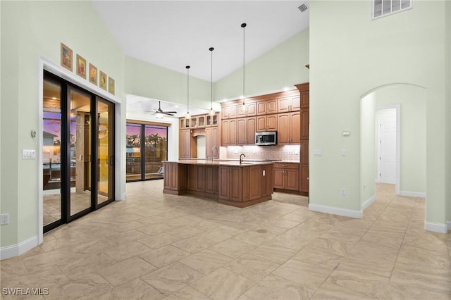 kitchen with pendant lighting, high vaulted ceiling, a center island with sink, decorative backsplash, and ceiling fan