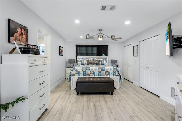 bedroom with ceiling fan, light hardwood / wood-style floors, and two closets