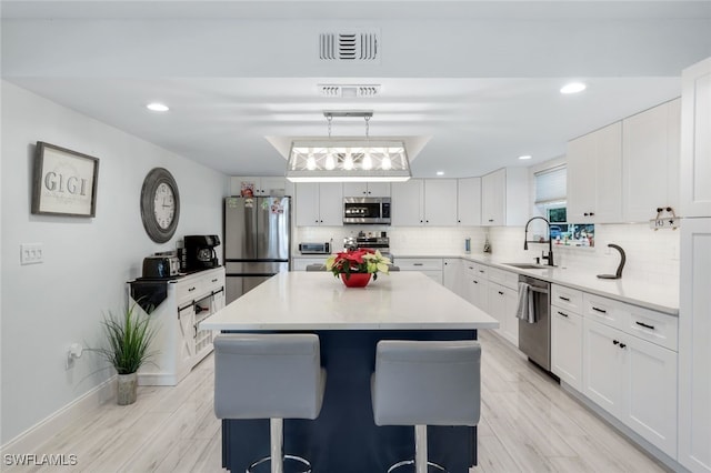 kitchen featuring appliances with stainless steel finishes, a breakfast bar, a kitchen island, sink, and white cabinetry