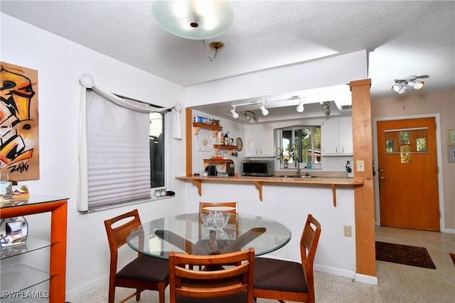 dining space with a textured ceiling, track lighting, and sink