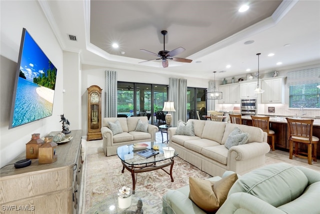 living room with ceiling fan, ornamental molding, a wealth of natural light, and a tray ceiling