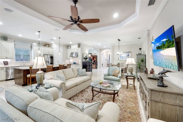 living room with ceiling fan with notable chandelier, a tray ceiling, and ornamental molding