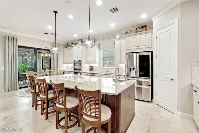 kitchen with light stone countertops, appliances with stainless steel finishes, pendant lighting, and an island with sink