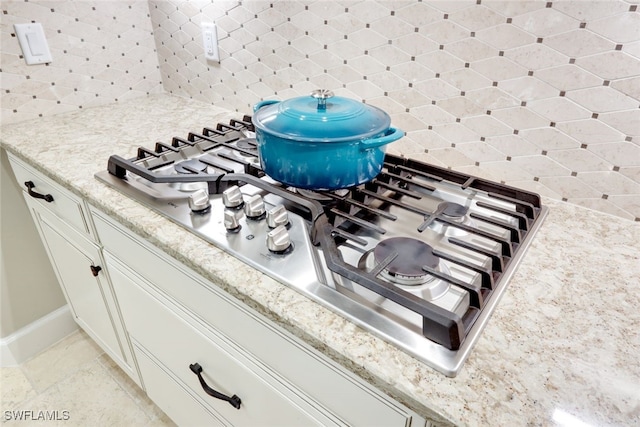 room details with stainless steel gas stovetop, white cabinetry, and backsplash