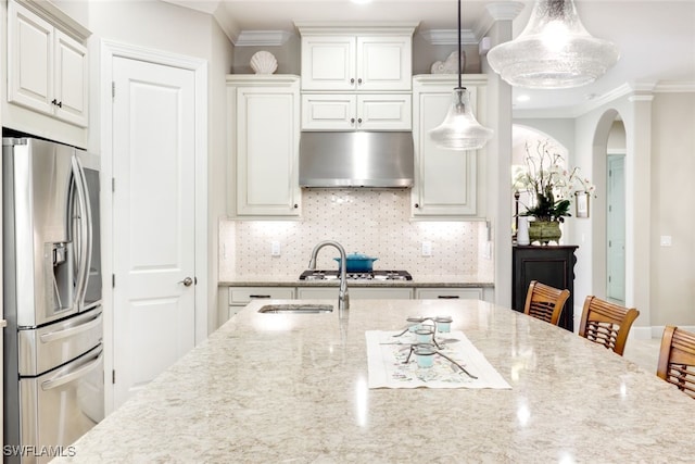 kitchen featuring wall chimney range hood, light stone counters, decorative light fixtures, decorative backsplash, and appliances with stainless steel finishes