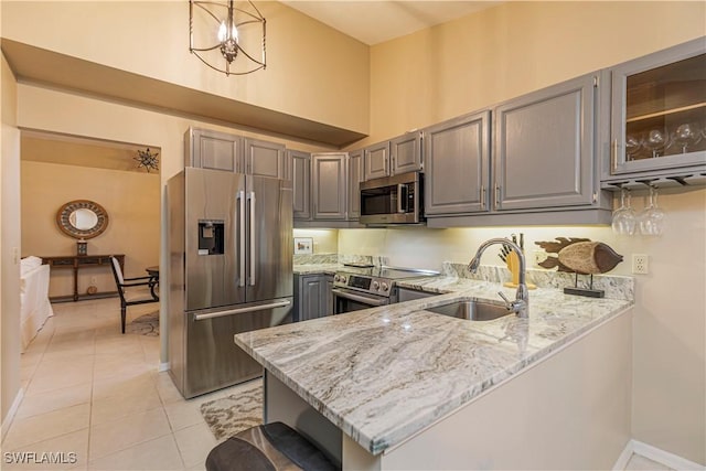 kitchen with kitchen peninsula, appliances with stainless steel finishes, light stone counters, sink, and hanging light fixtures