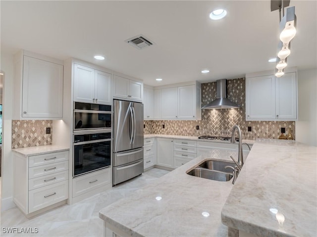 kitchen with visible vents, wall chimney exhaust hood, light stone counters, stainless steel appliances, and a sink