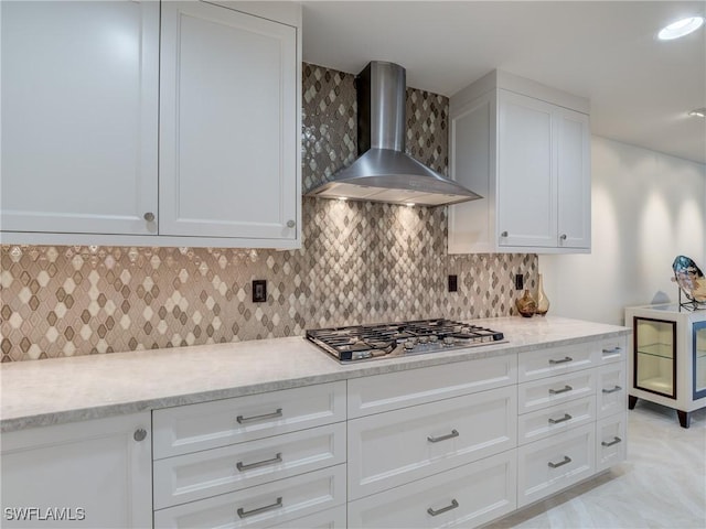 kitchen featuring stainless steel gas cooktop, decorative backsplash, white cabinetry, light stone countertops, and wall chimney exhaust hood