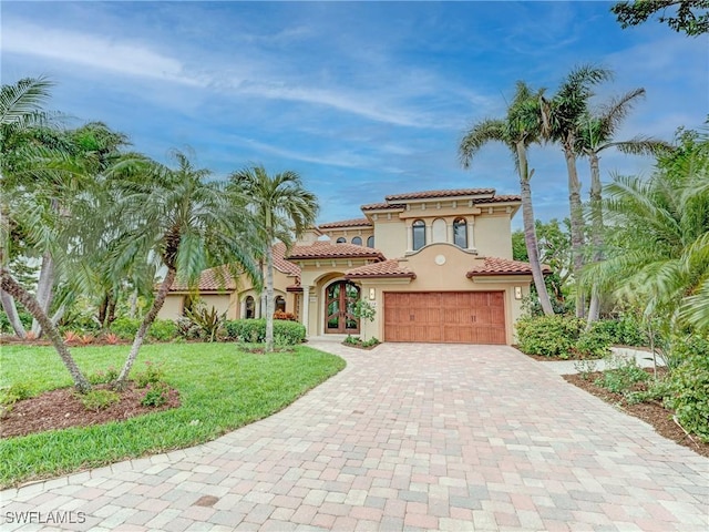 mediterranean / spanish-style home featuring stucco siding, a tiled roof, an attached garage, decorative driveway, and a front yard