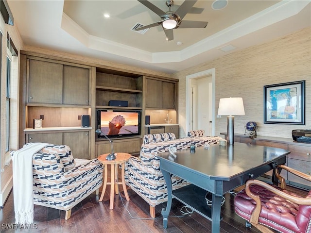 office area with ceiling fan, dark wood-style flooring, visible vents, ornamental molding, and a tray ceiling