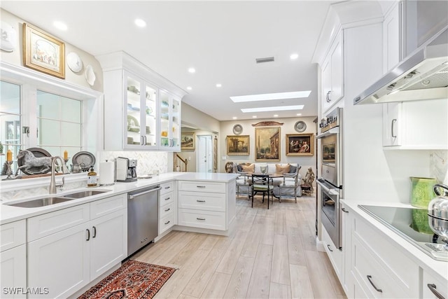 kitchen featuring appliances with stainless steel finishes, sink, white cabinets, and wall chimney range hood