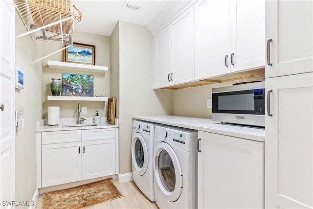 washroom with light wood-type flooring, sink, washing machine and clothes dryer, and cabinets