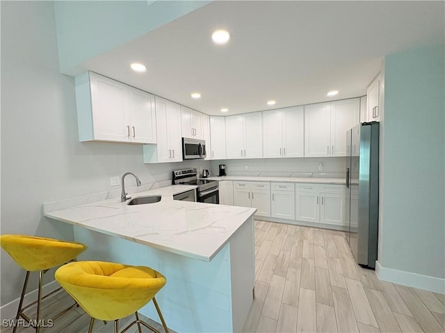 kitchen featuring kitchen peninsula, stainless steel appliances, sink, white cabinetry, and a breakfast bar area