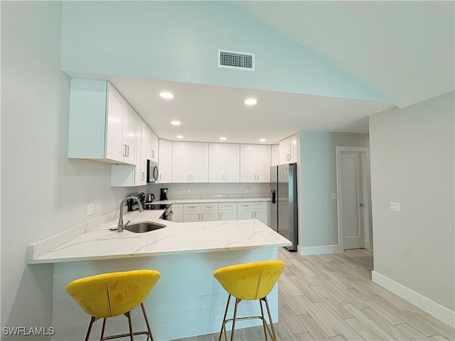 kitchen with a breakfast bar, sink, white cabinetry, kitchen peninsula, and stainless steel appliances