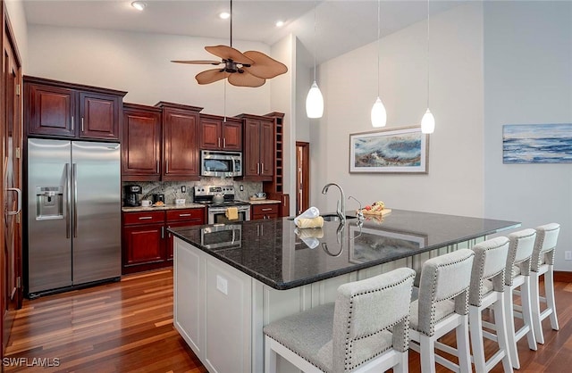 kitchen with backsplash, high vaulted ceiling, a center island with sink, appliances with stainless steel finishes, and dark hardwood / wood-style flooring