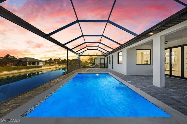 pool at dusk featuring a patio, a water view, and glass enclosure