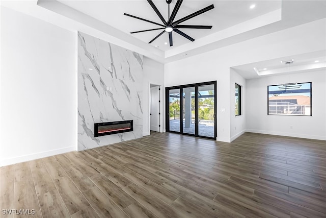 unfurnished living room featuring a raised ceiling, baseboards, a premium fireplace, and wood finished floors