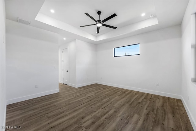 spare room featuring a raised ceiling, ceiling fan, and dark wood-type flooring