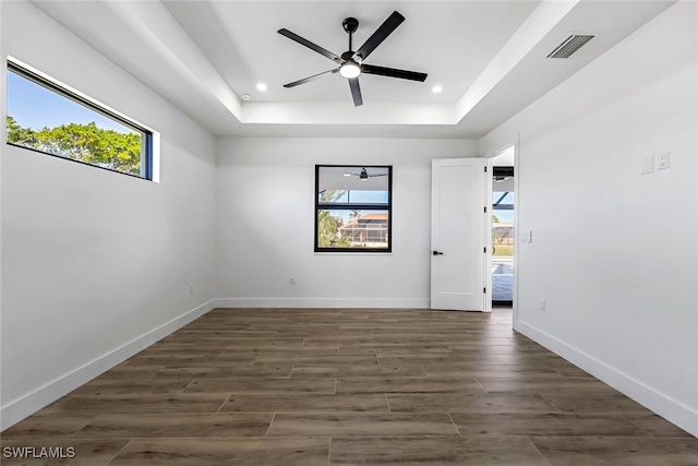 empty room with a raised ceiling, ceiling fan, and dark hardwood / wood-style floors