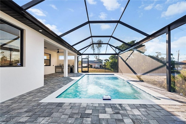 pool with glass enclosure, ceiling fan, a patio area, and area for grilling