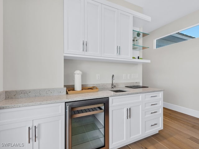 kitchen with sink, wine cooler, light stone counters, light hardwood / wood-style flooring, and white cabinets