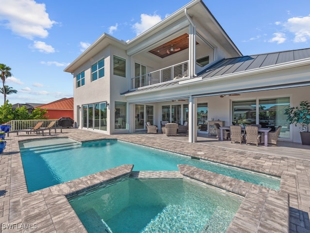 rear view of property with a patio, a balcony, ceiling fan, and a pool with hot tub