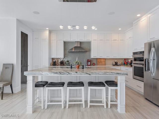 kitchen featuring appliances with stainless steel finishes, white cabinetry, a kitchen island with sink, and wall chimney exhaust hood