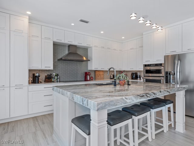 kitchen with a breakfast bar, a center island with sink, stainless steel appliances, and wall chimney range hood