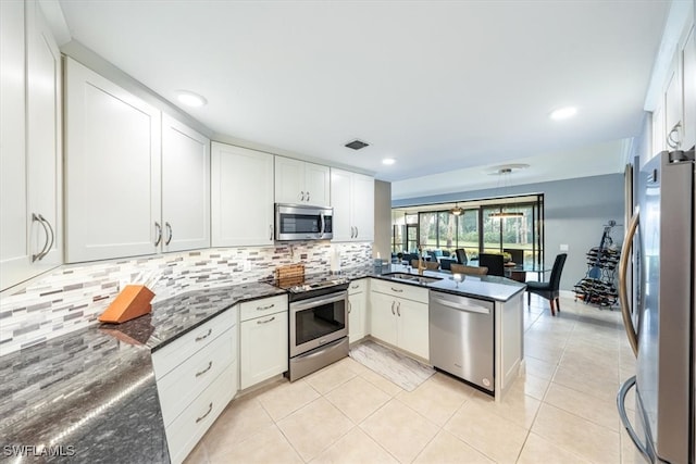 kitchen with kitchen peninsula, white cabinetry, dark stone counters, and appliances with stainless steel finishes