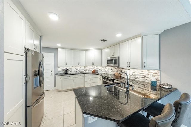 kitchen featuring stainless steel appliances, kitchen peninsula, dark stone countertops, decorative backsplash, and white cabinets