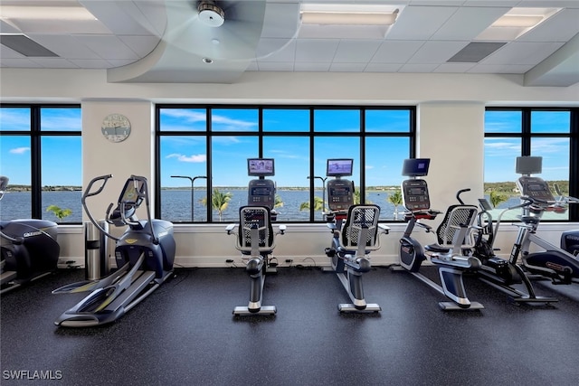 gym with a paneled ceiling, ceiling fan, and a water view