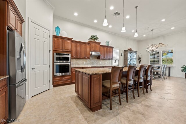 kitchen with appliances with stainless steel finishes, light stone counters, ornamental molding, a kitchen island with sink, and hanging light fixtures