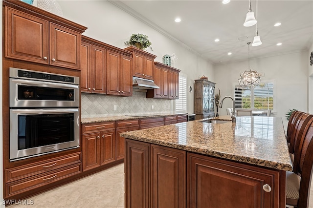 kitchen with an inviting chandelier, crown molding, an island with sink, decorative light fixtures, and stainless steel double oven